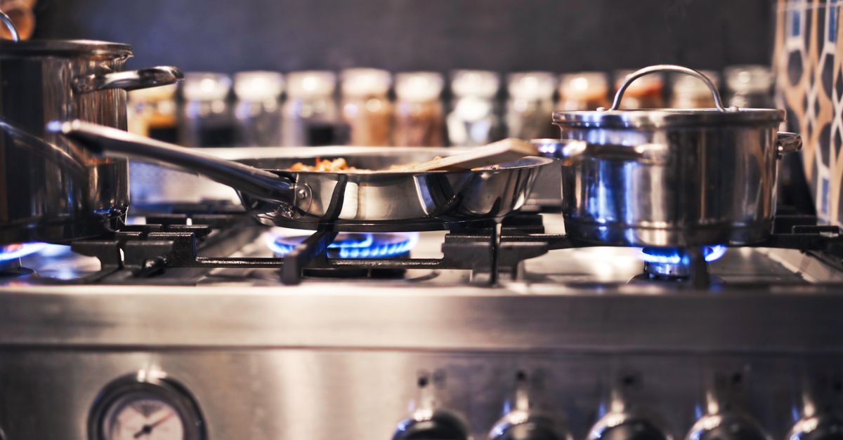 Cooking utensils including pots and pans on a gas stove with blue flames.