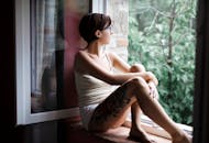 一名短发纹身的女子坐在窗前，望着外面沉思