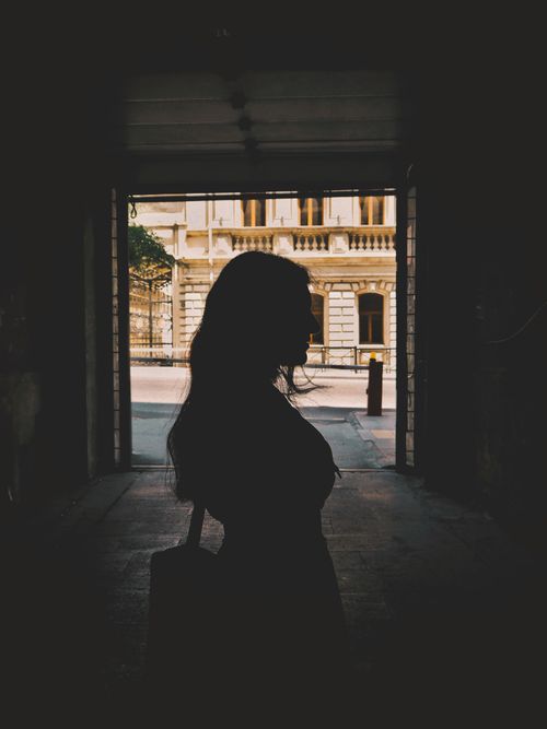 Free Silhouette of a woman standing in a shadowed urban passageway with sunlight outside. Stock Photo
