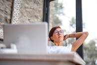 一位戴眼镜的女人坐在办公桌前，若有所思地凝视着窗外