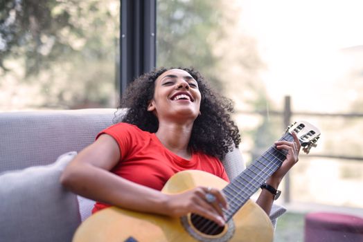 Smiling woman enjoying music while playing an acoustic guitar indoors, creating a happy and relaxed ambiance.