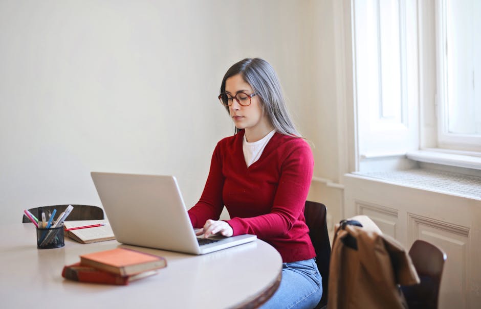 Woman in Red Long Sleeve Shirt Sitting on Chair Using Macbook