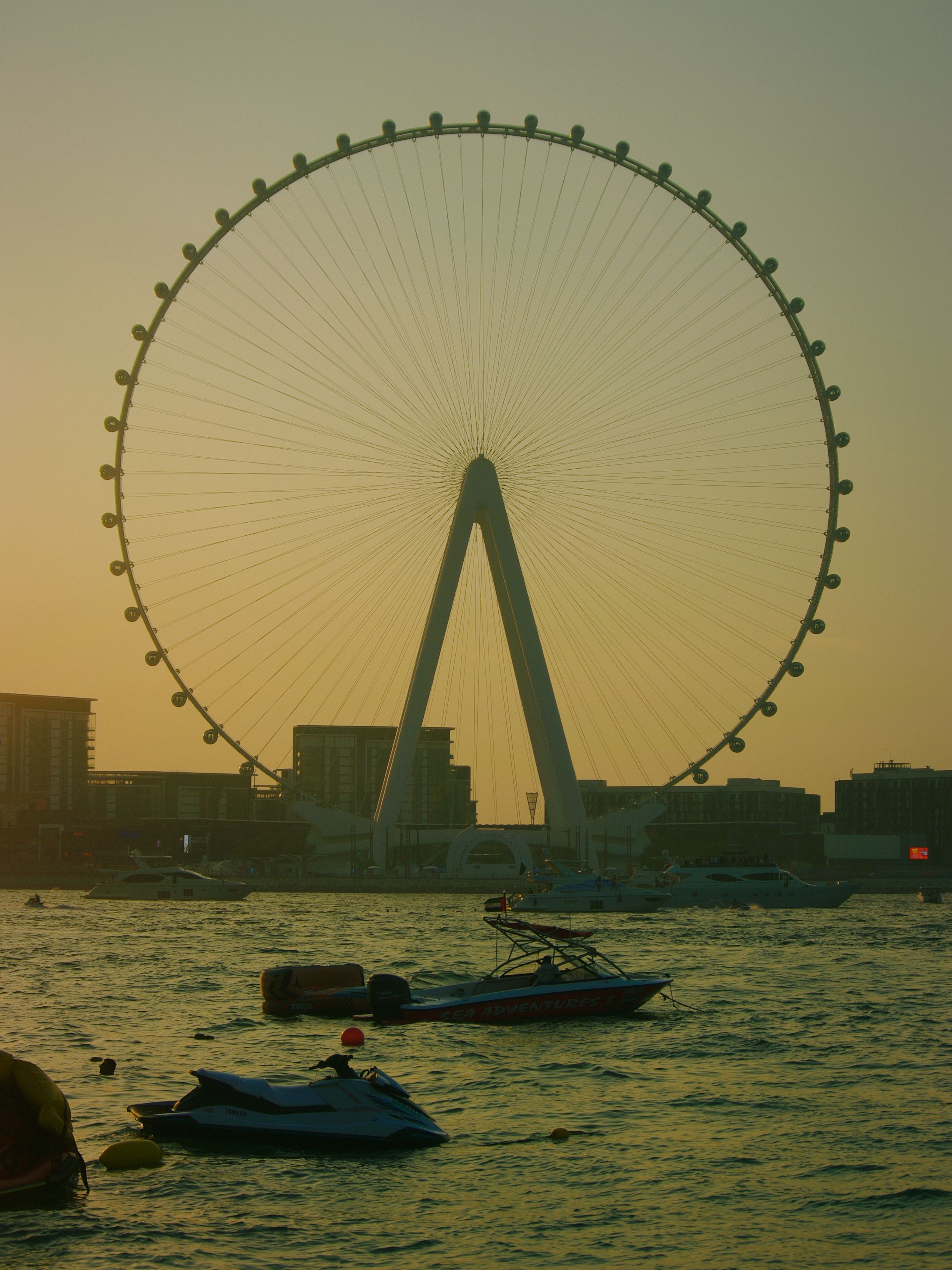 Silhouette of a ferris wheel and boats at sunset by the waterfront.