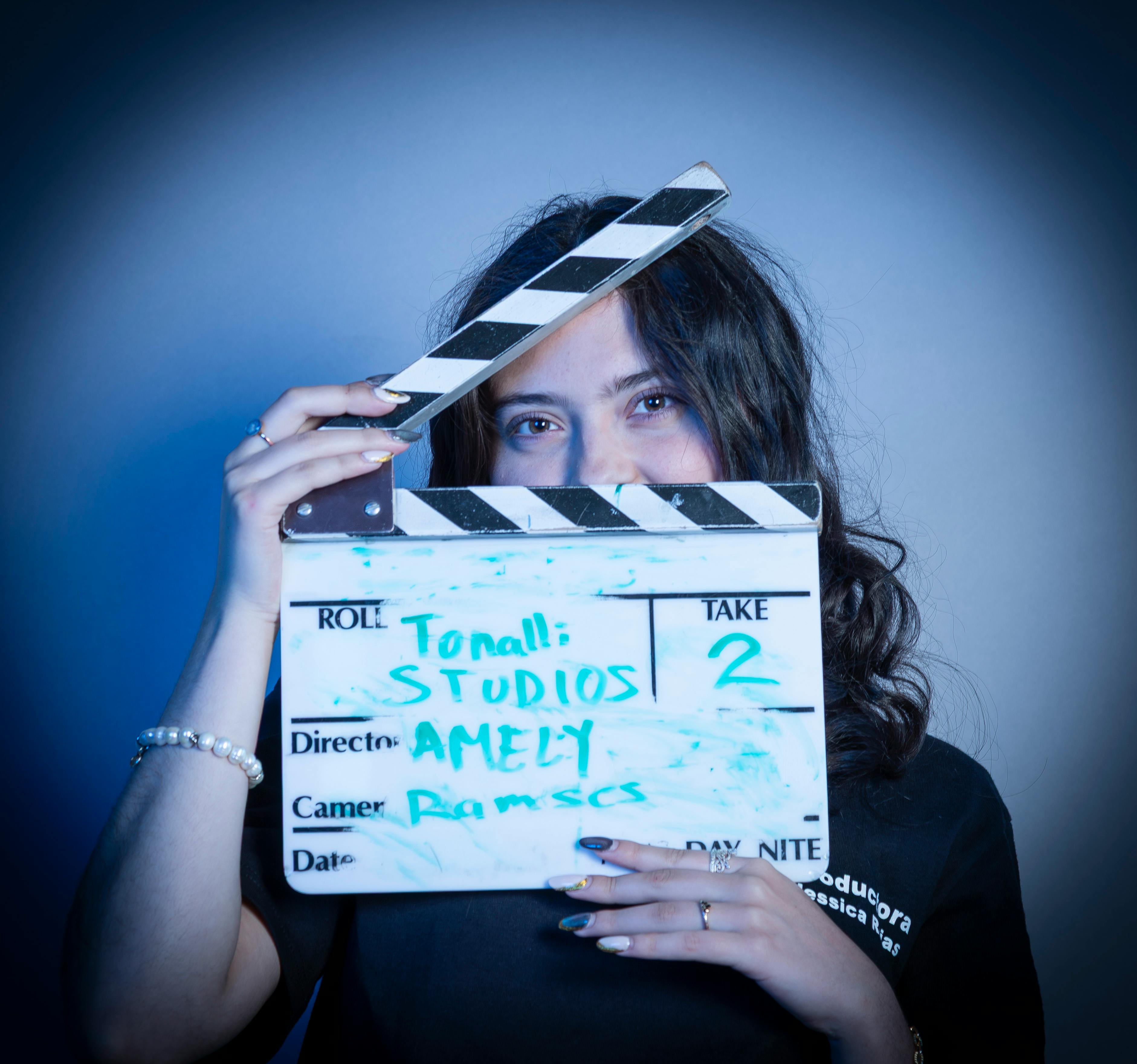 Female director holding a clapperboard in a film studio with blue lighting.