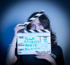 Female director holding a clapperboard in a film studio with blue lighting.