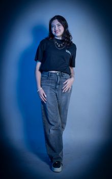 Confident young woman posing in a stylish denim and tee outfit with blue lighting.