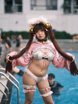A person in a pink cosplay costume poses by a pool at an event in Vietnam.