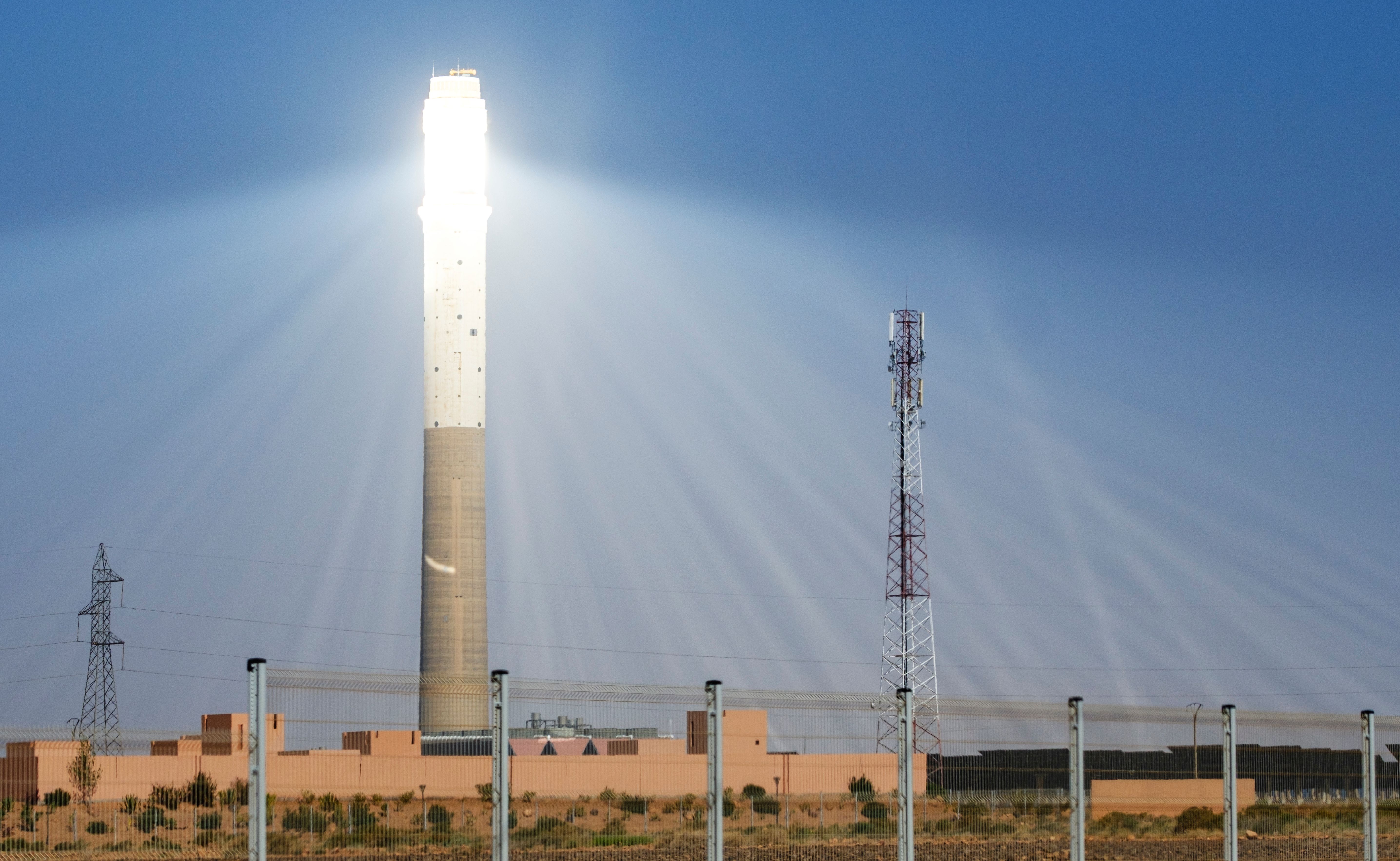Solar power tower illuminated under a clear blue sky.
