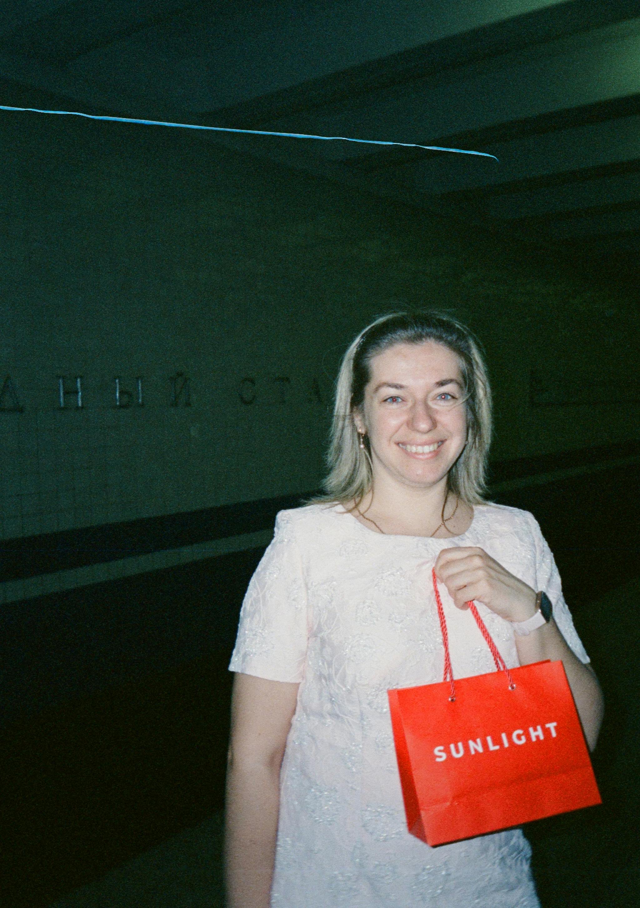 Woman in a subway station holding a Sunlight bag, smiling.