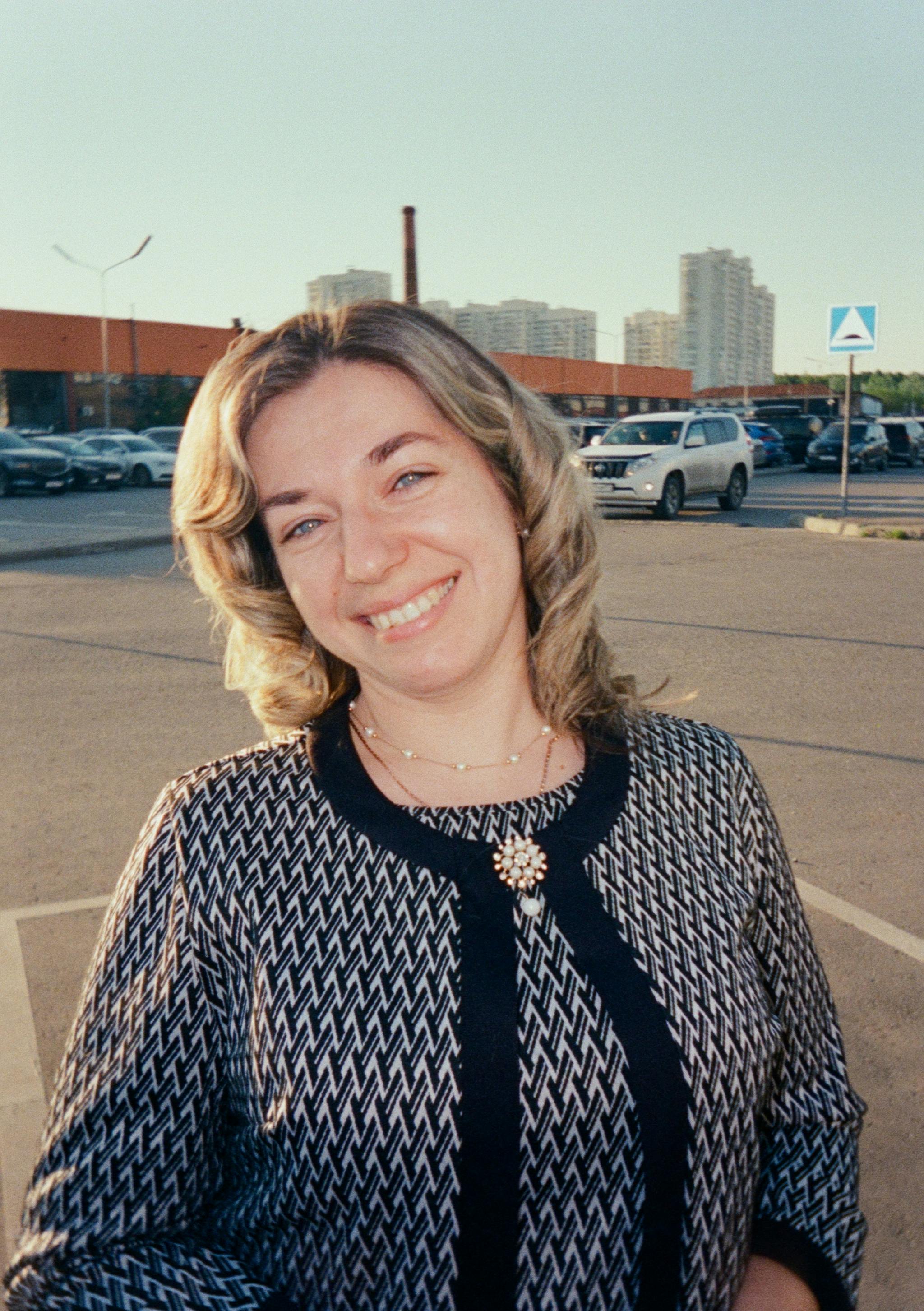 Portrait of a woman smiling in a sunny urban environment with buildings in the background.