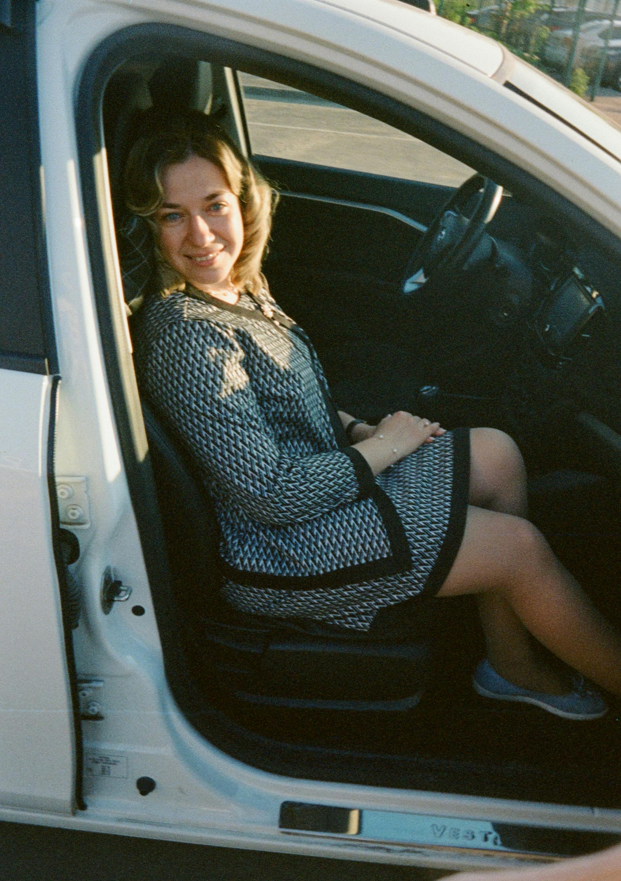 Woman seated in a car, smiling towards the camera with the door open.