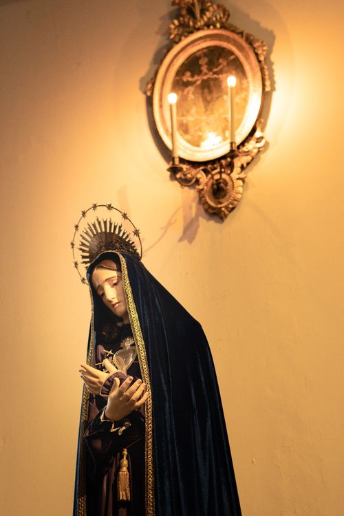 Free Candlit statue of Virgin Mary with halo, praying inside a church, evoking peace and spirituality. Stock Photo