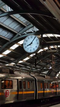 A busy city train station with a large clock and moving train under a metal roof.