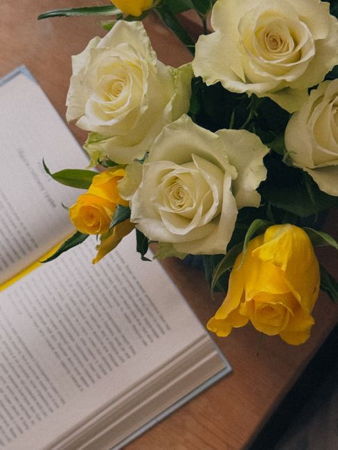 A beautiful bouquet of yellow and white roses beside an open book on a wooden table.