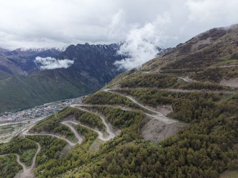 Aerial view of winding roads on a lush mountain landscape with snow-capped peaks in the background.