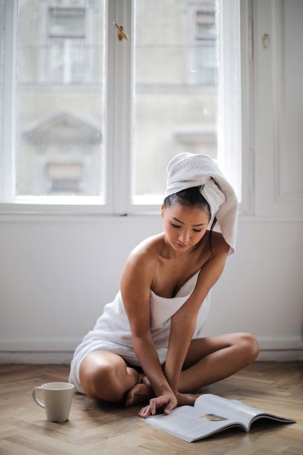 A woman wrapped in a towel reads by a window, epitomizing comfort and relaxation with a warm drink by her side.
