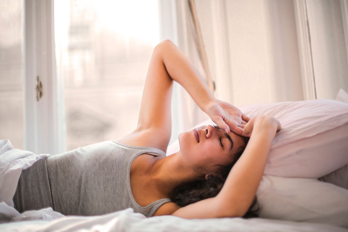Femme allongée dans son lit, la main sur le front, réveillée au milieu de la nuit