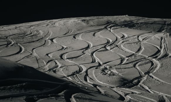 Detailed view of ski tracks forming patterns on a snowy mountain slope under bright daylight.