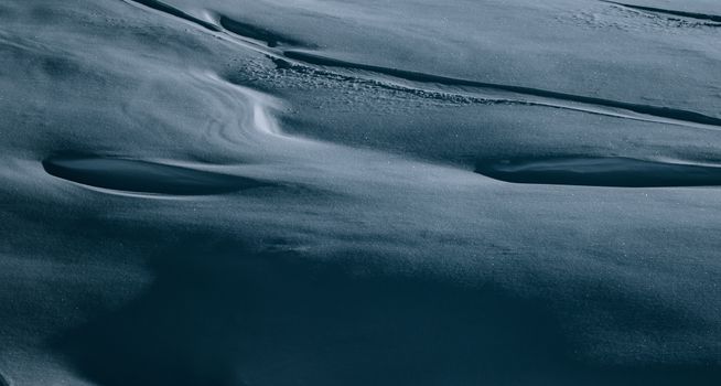 An intricate aerial shot of rippling snow patterns under cool lighting in winter.
