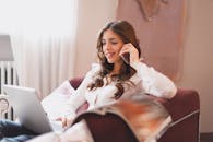 一位女士在舒适的室内环境中，微笑着同时用手机和笔记本电脑处理多项任务