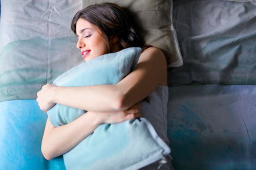 бесплатная Женщина, лежа на кровати, обнимая подушку Стоковое фото