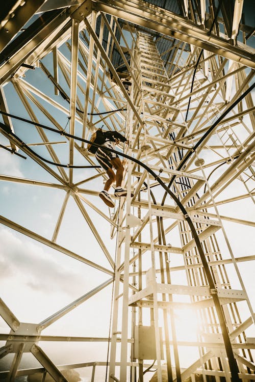 Anonymous person climbing metal tower on sunny day