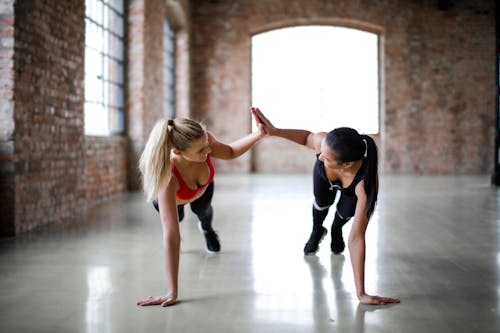 Young slender female athletes giving high five to each other while training together in sports club