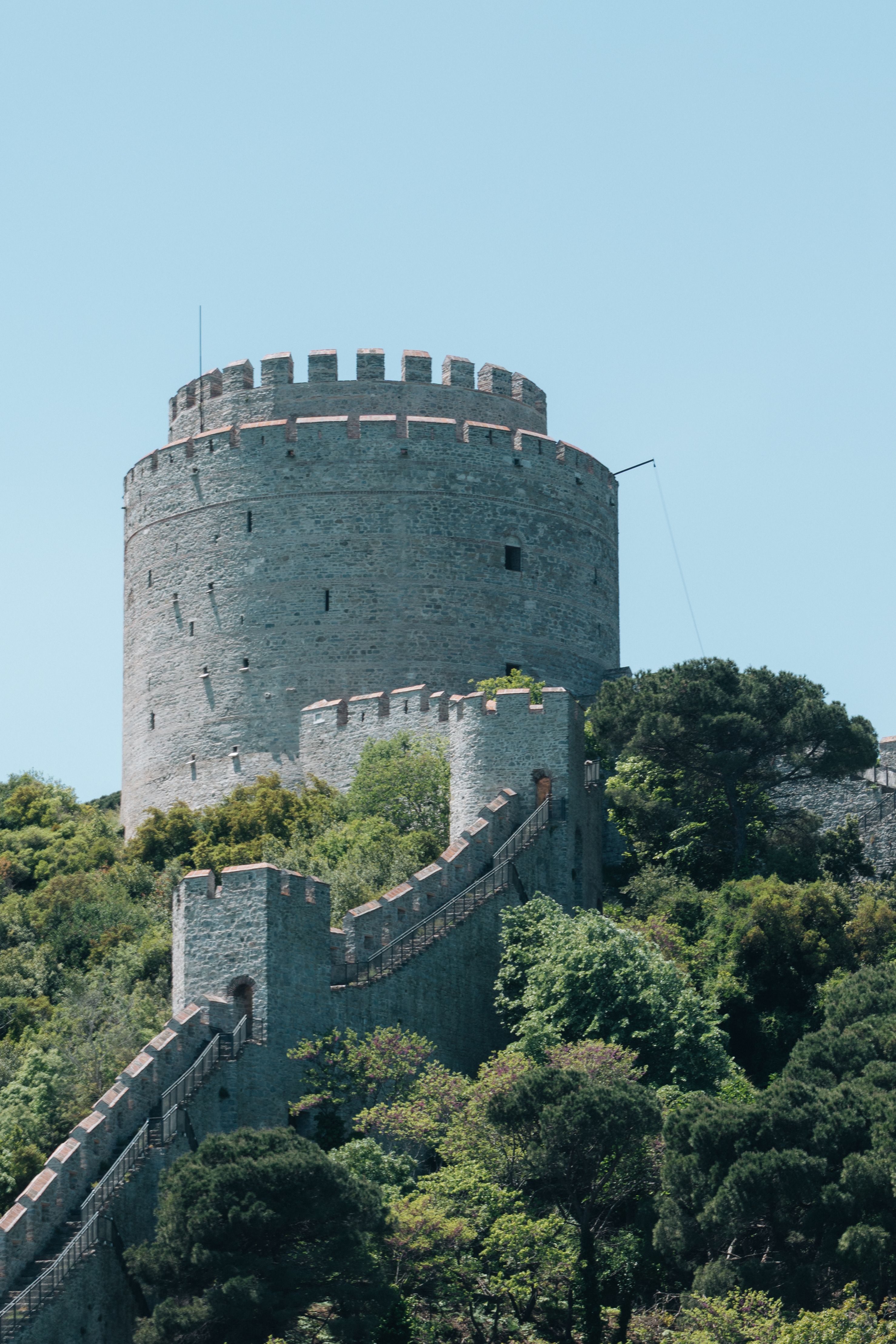 A majestic stone tower stands tall amid lush greenery, showcasing medieval architecture in daylight.