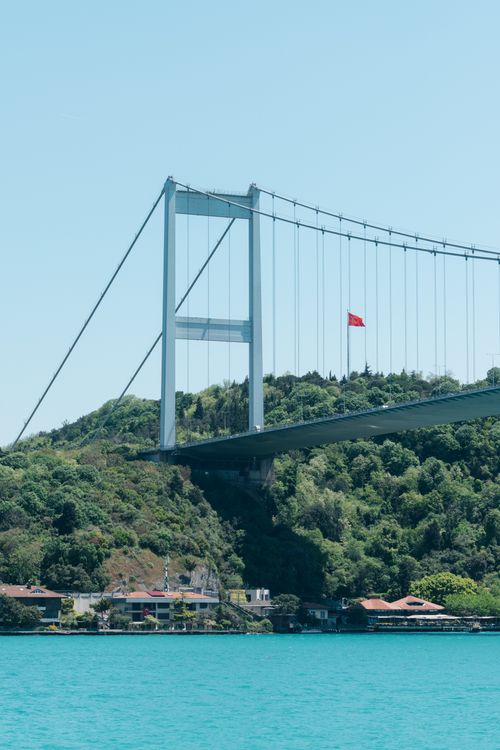 Free A stunning view of the Bosphorus Bridge spanning over turquoise waters with a Turkish flag visible. Stock Photo