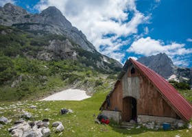 Brown Wooden House Near Green Mountain Under White Clouds