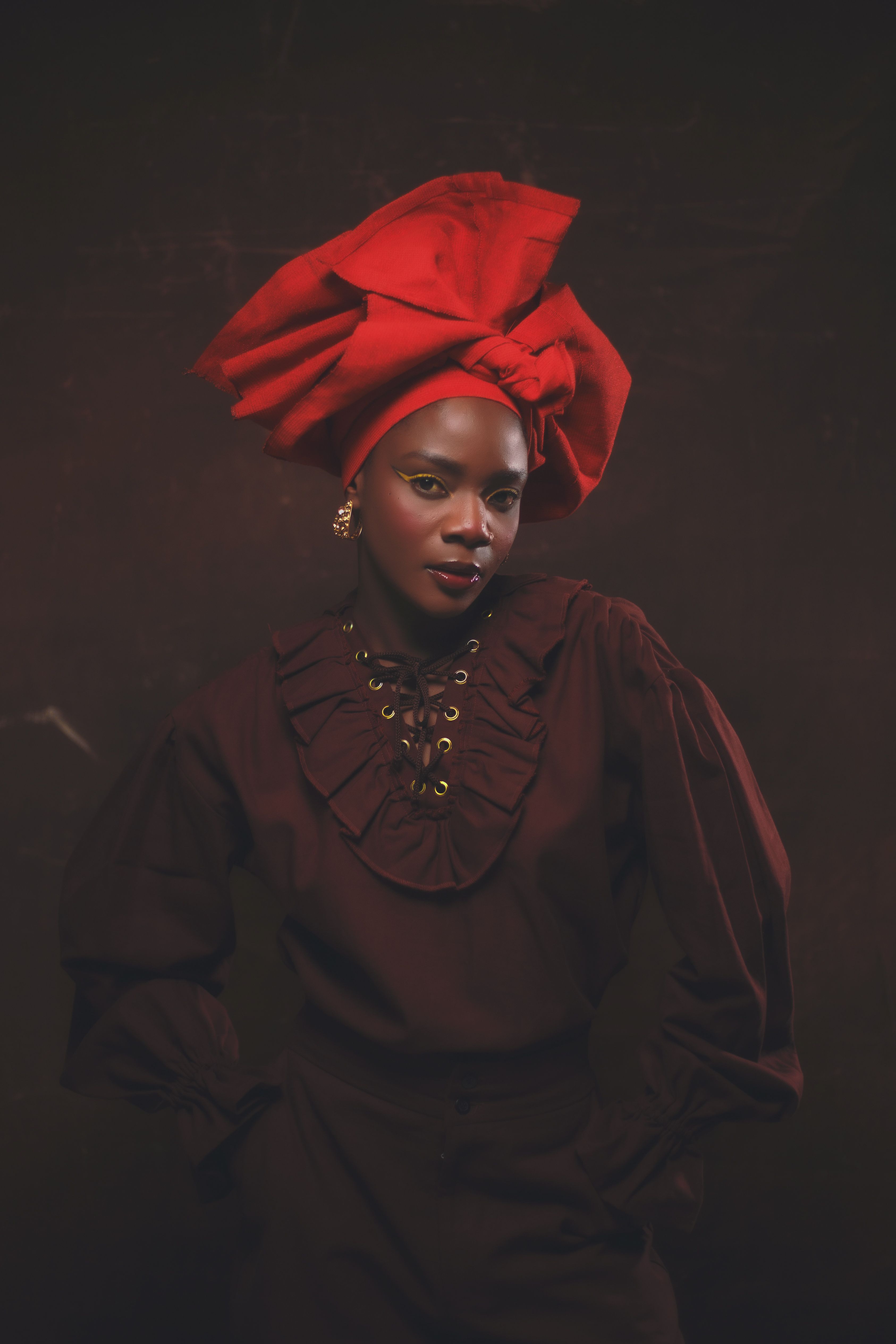 Portrait of a woman in traditional Nigerian attire, wearing a vibrant red headwrap.