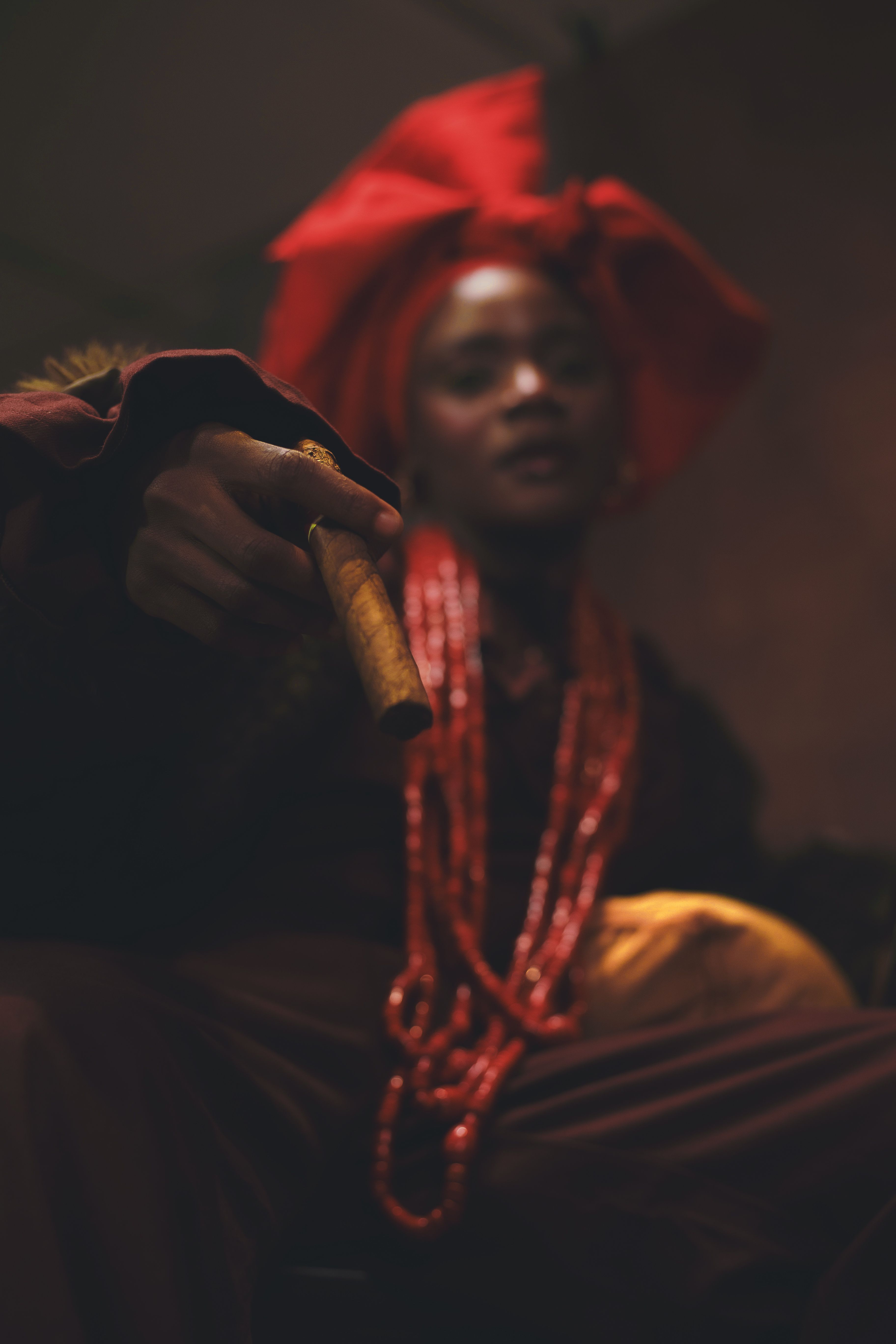 Person in traditional attire with a red headwrap and beads, holding a cane in Nigeria.
