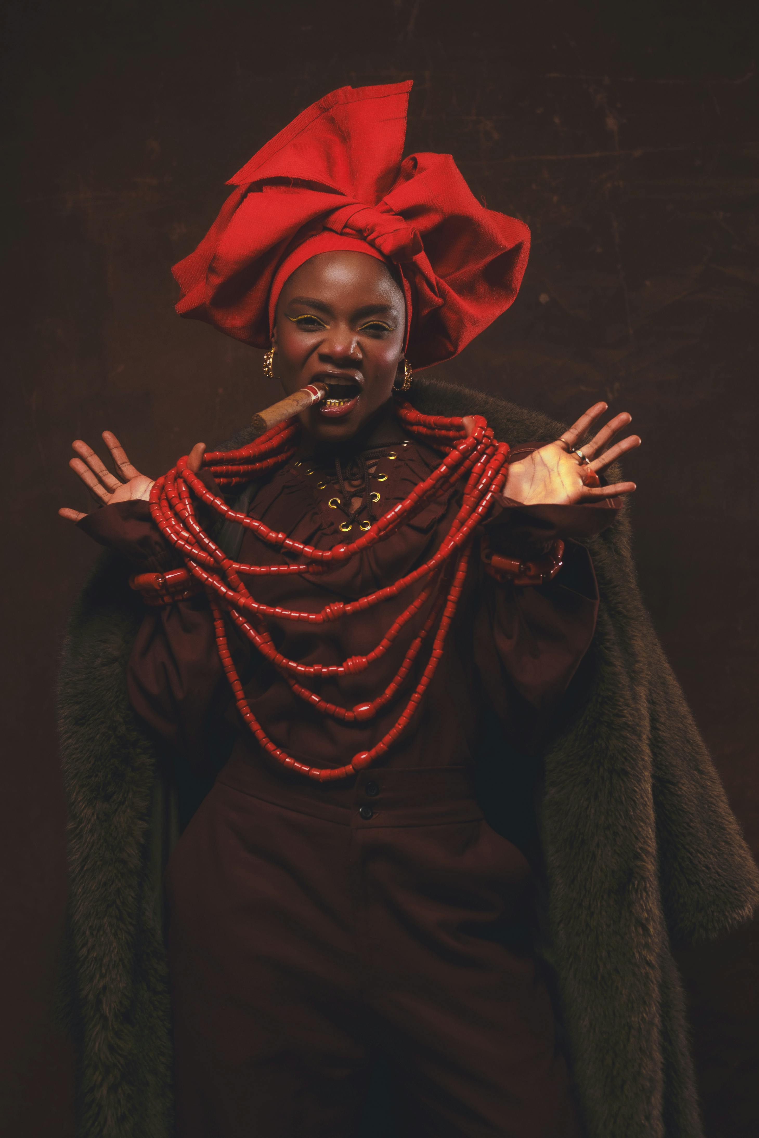 Portrait of a woman in traditional Nigerian attire, featuring a vibrant red gele and coral necklace.