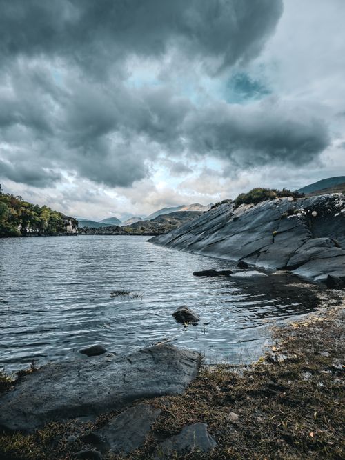 Free Dramatic cloudy sky over a lake and rocky shore in Irish landscape, ideal for travel and nature themes. Stock Photo