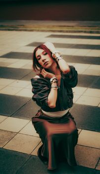 Fashionable woman sitting and posing on a checkered pavement. Moody and artistic composition.