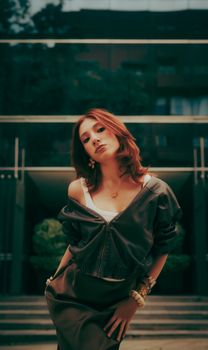 Stylish woman with red hair modeling in an urban setting, showcasing modern fashion.
