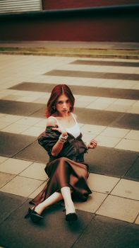 Stylish woman sits on urban striped pavement, exuding modern fashion vibes