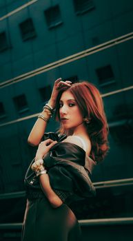 Elegant woman with red hair poses confidently outdoors against a modern building backdrop.