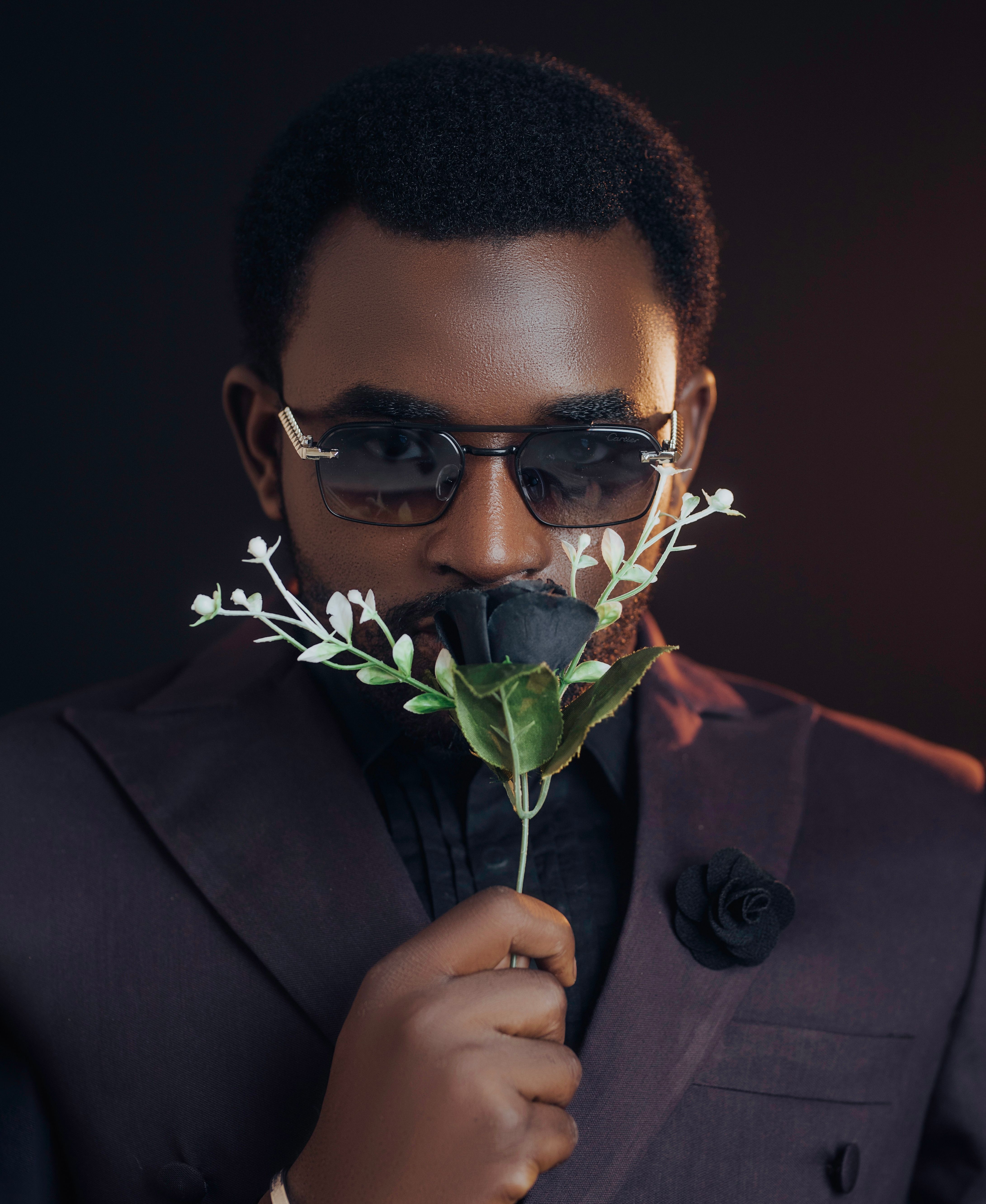 Stylish portrait of an adult man in sunglasses, holding a black rose. Modern fashion in a dark setting.