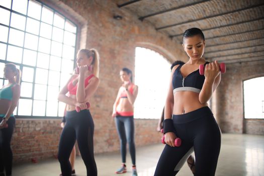 Women exercising with dumbbells in a stylish loft studio, showcasing fitness and active lifestyle.