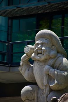 A detailed statue of a Japanese deity with a mallet in front of a modern building facade.