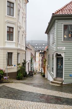 Rainy narrow street in Bergen, Norway, featuring colorful houses and cobblestone paving.