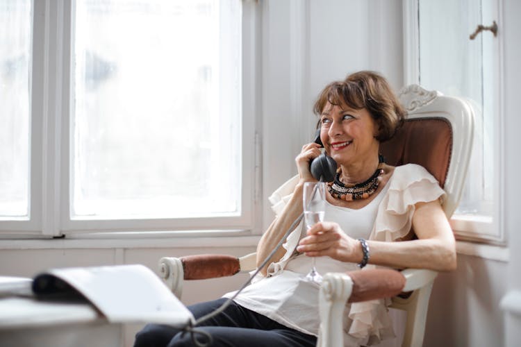 Happy Middle Aged Woman Making Phone Call And Drinking Tasty At Home