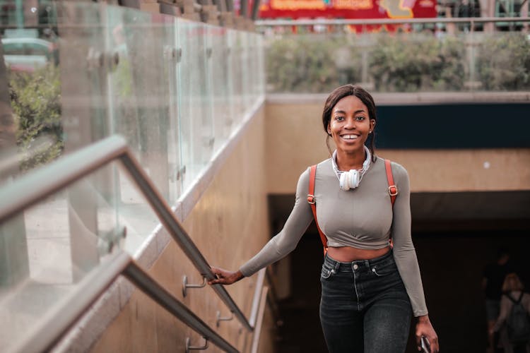 Photo Of Smiling Woman In Gray Top And Black Denim Jeans Walking Up Some Stairs