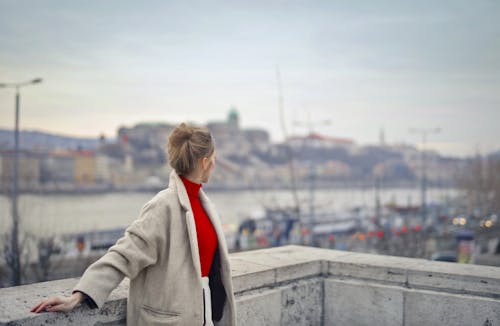 Free Selective Focus Photo of Woman in Winter Coat Standing against Concrete Railing Looking Away Stock Photo