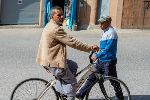 Free A man rides a bicycle on a sunny urban street, passing a pedestrian. Stock Photo