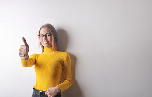 Foto De Mulher Em Suéter Amarelo De Gola Alta, Jeans Azul E óculos Mostrando Os Polegares Para Cima