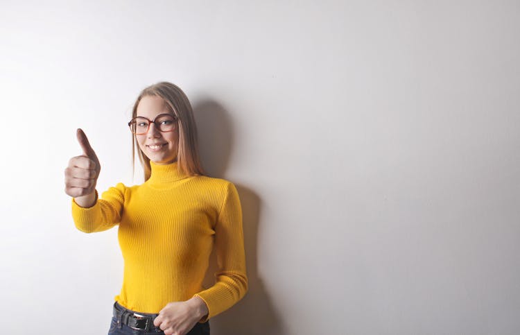 Photo Of Woman In Yellow Turtleneck Sweater, Blue Denim Jeans, And Glasses Giving The Thumbs Up