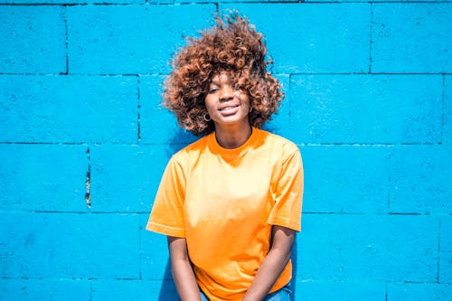 Foto Van Glimlachende Vrouw In Oranje T Shirt Die Op Blauwe Muur Leunt