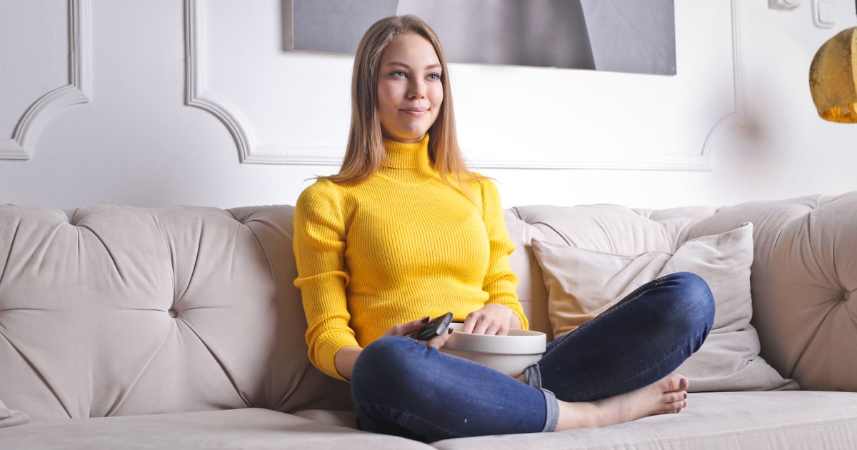 A woman relaxing on a sofa at home with a remote control.